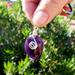 Deep purple Amethyst keychain with silver wire wrap, shown in close up outdoors in front of green bush for natural contrast.